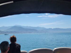 View of Puerto Vallarta mountains and ocean, photo taken of the shore from a boat in motion, silloutte of a person gazing out into the beauty of the water and blue hue mountains